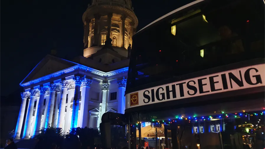 Sightseeingbus vor einer beleuchteten Berliner Kirche bei Nacht